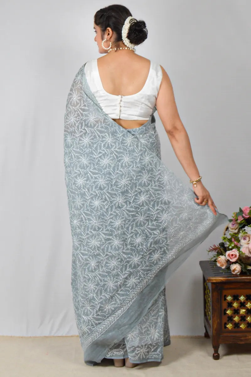 Woman wearing a light blue saree with white patterns, standing against a plain background.