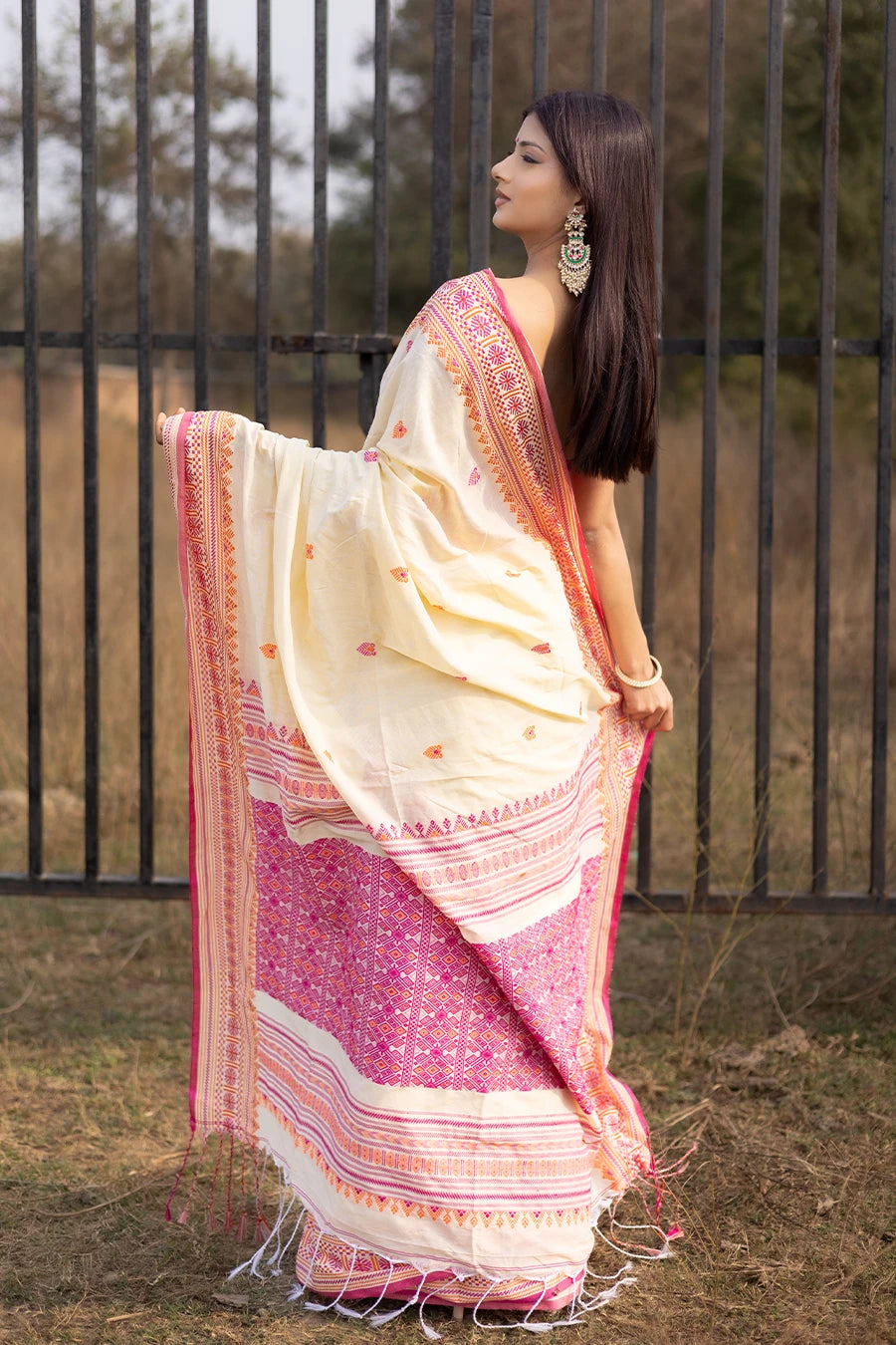 Woman wearing a white and pink saree with a black metal gate in the background