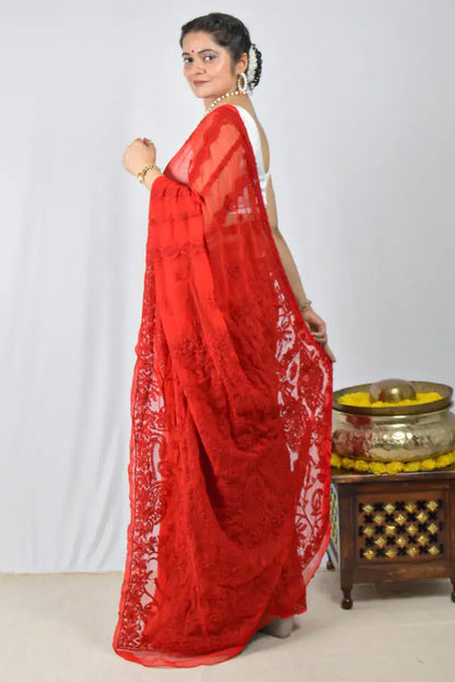 Woman wearing a red saree with white patterns on a plain background