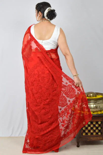 Woman wearing a red saree with white patterns on a plain background