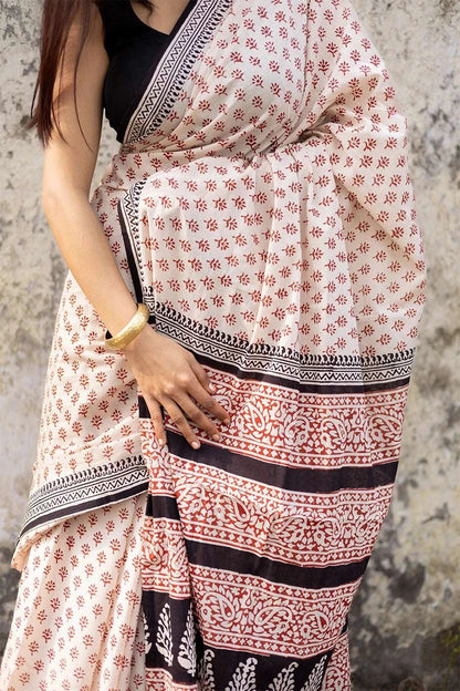 Woman wearing a patterned saree against a textured wall.