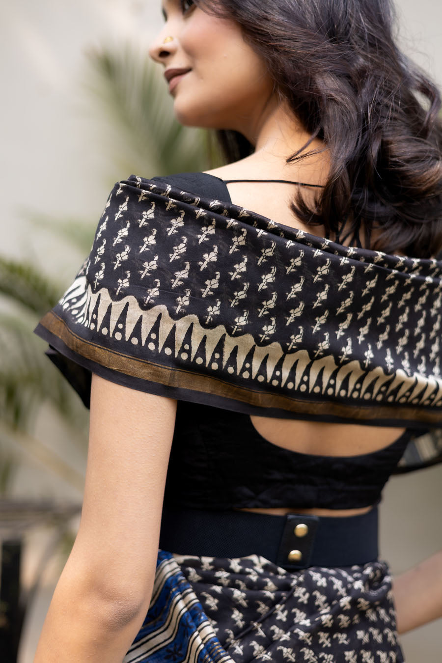 Model wearing a black designer printed saree with woven motifs, blue striped pallu, and a modern belted drape suitable for festive and party wear.