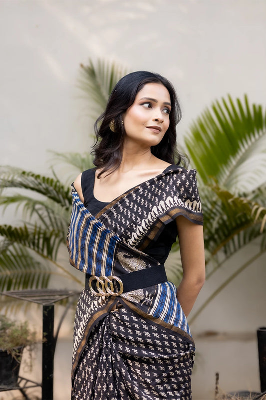 Model wearing a black designer printed saree with woven motifs, blue striped pallu, and a modern belted drape suitable for festive and party wear.
