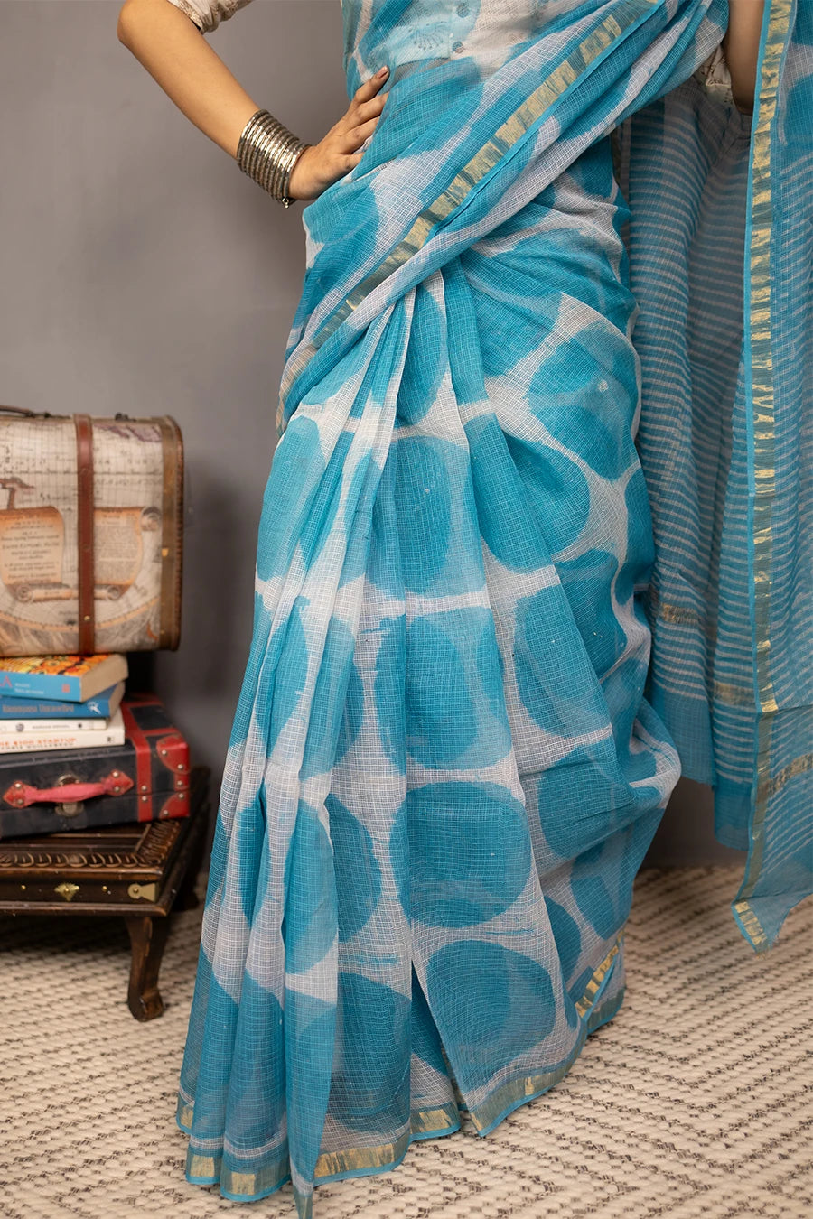 Woman in a blue saree with white patterns standing against a grey wall.