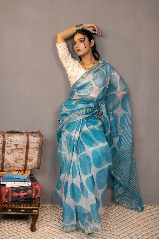 Woman in a blue saree with white patterns standing against a grey wall.