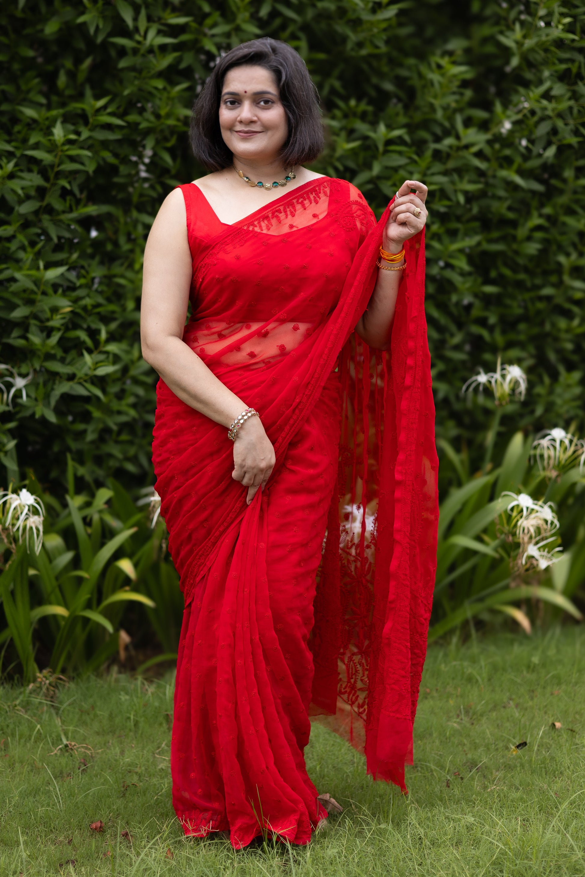 Woman wearing red georgette Lucknowi chikankari saree with blouse, front pose in garden