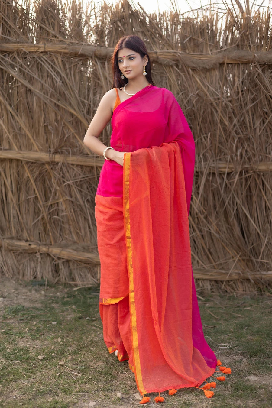 Model wearing a magenta and orange mul cotton saree with contrast border and tassel detailing, suitable for daily wear, casual outings, and festive occasions.