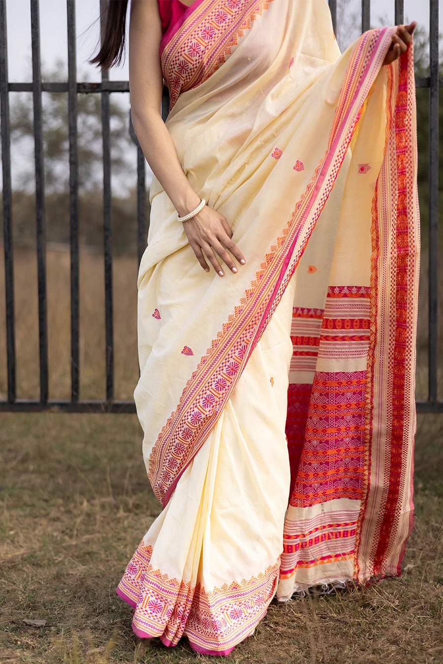 Woman wearing a white and pink saree with a black metal gate in the background