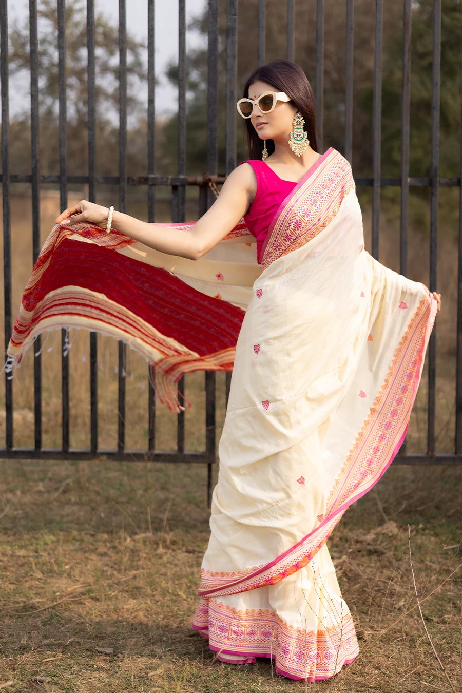 Woman wearing a white and pink saree with a black metal gate in the background