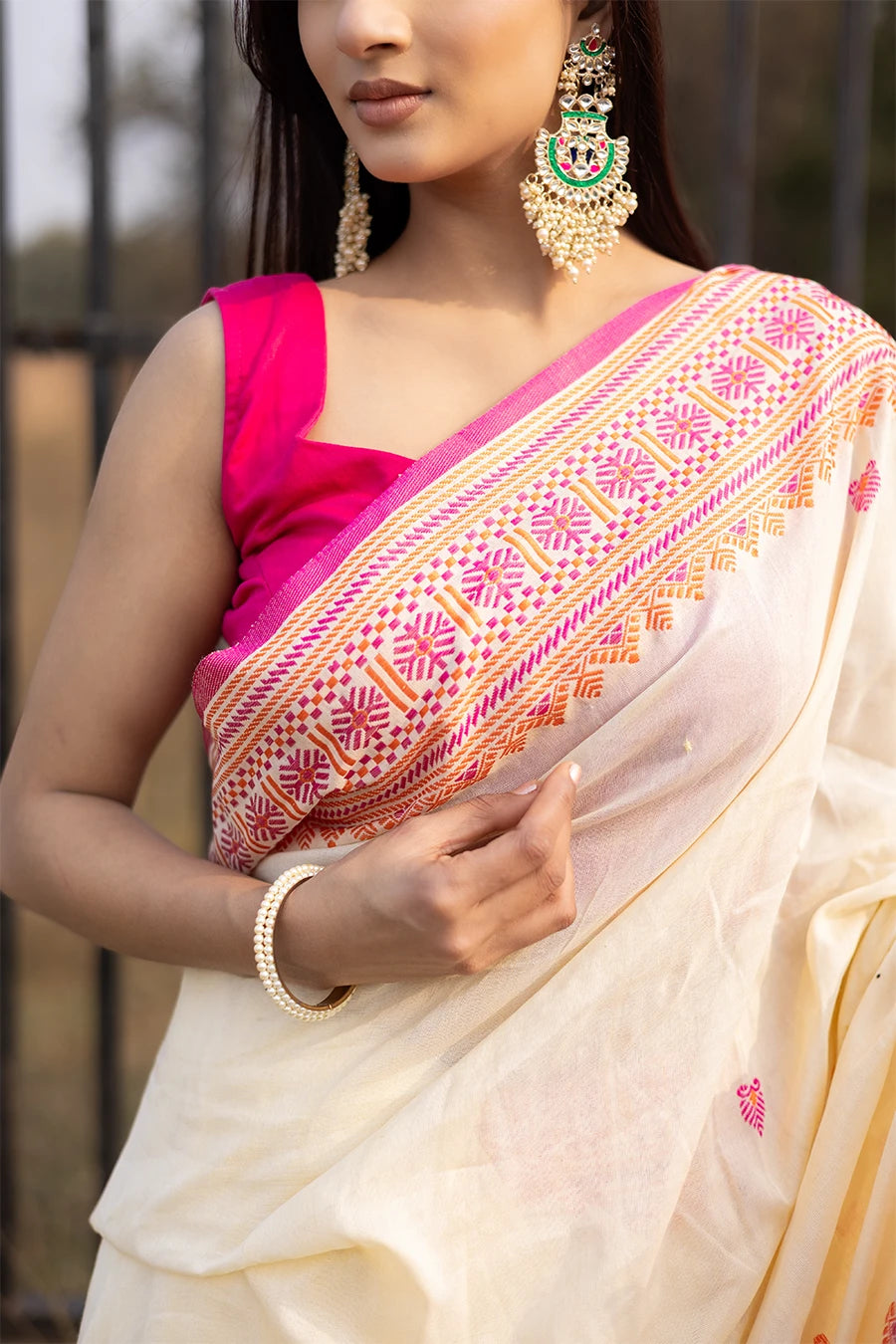 Woman wearing a white and pink saree with a black metal gate in the background