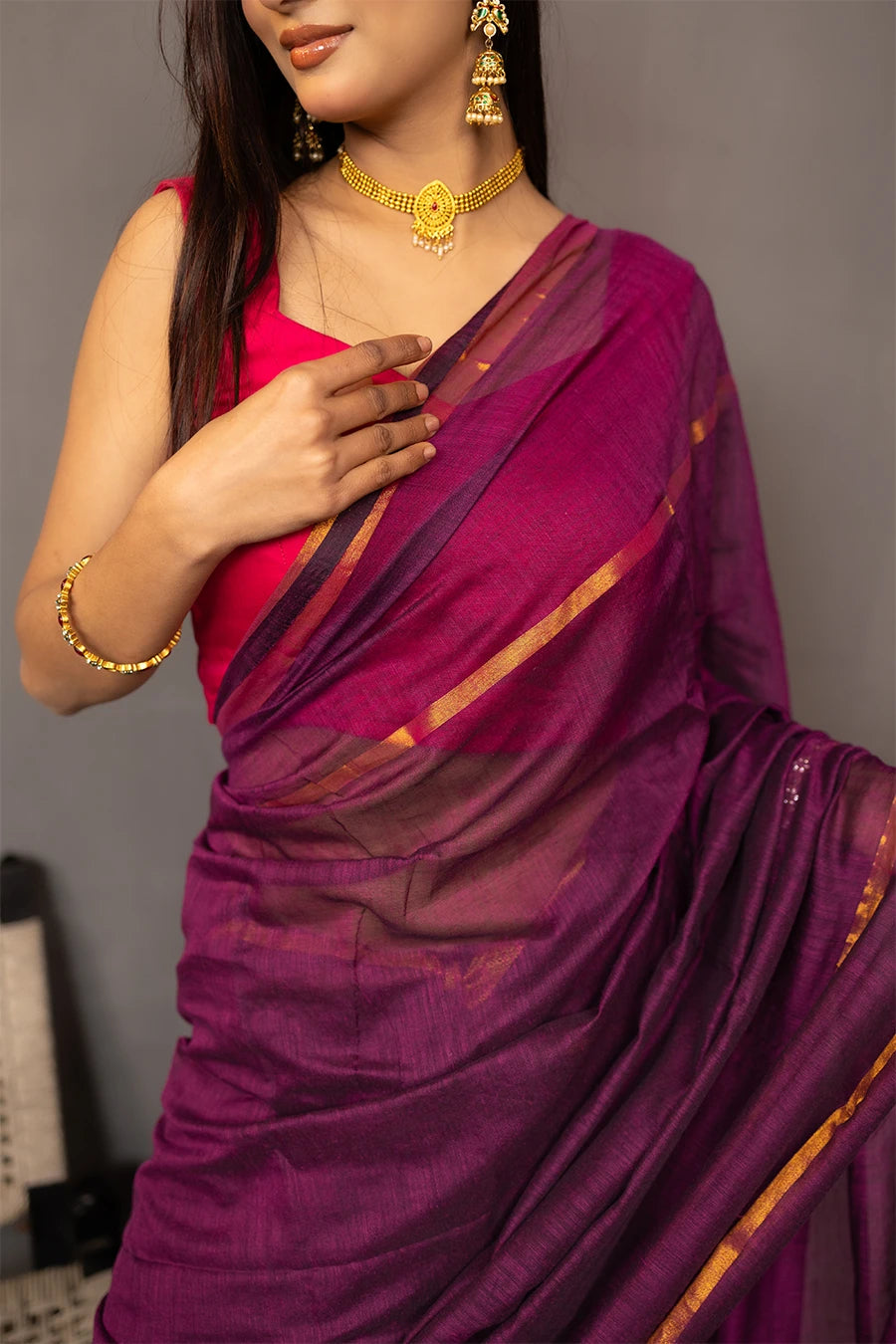 Woman wearing a purple saree with a red blouse against a grey background