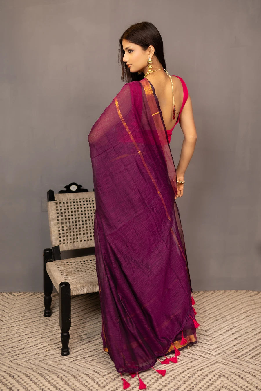 Woman wearing a purple saree with a red blouse against a grey background