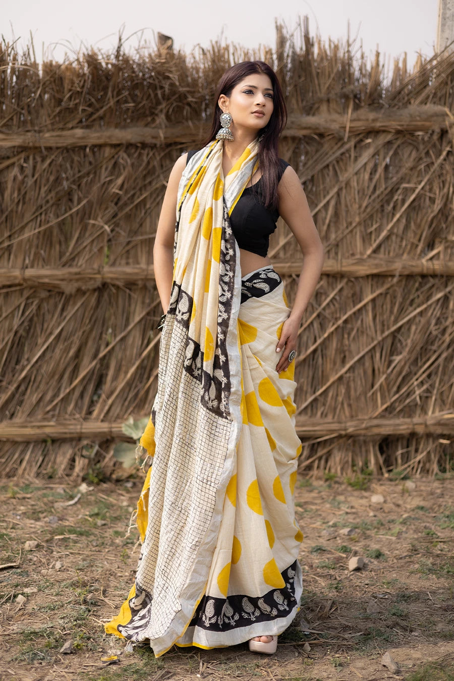 Woman wearing a traditional saree with yellow and white pattern in front of a rustic background