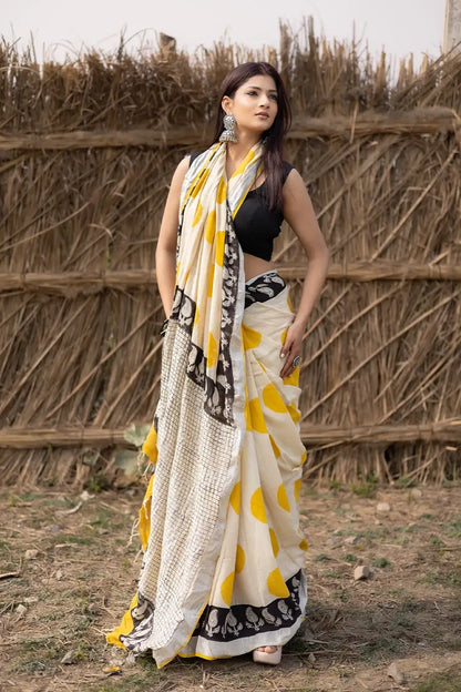 Woman wearing a traditional saree with yellow and white pattern in front of a rustic background