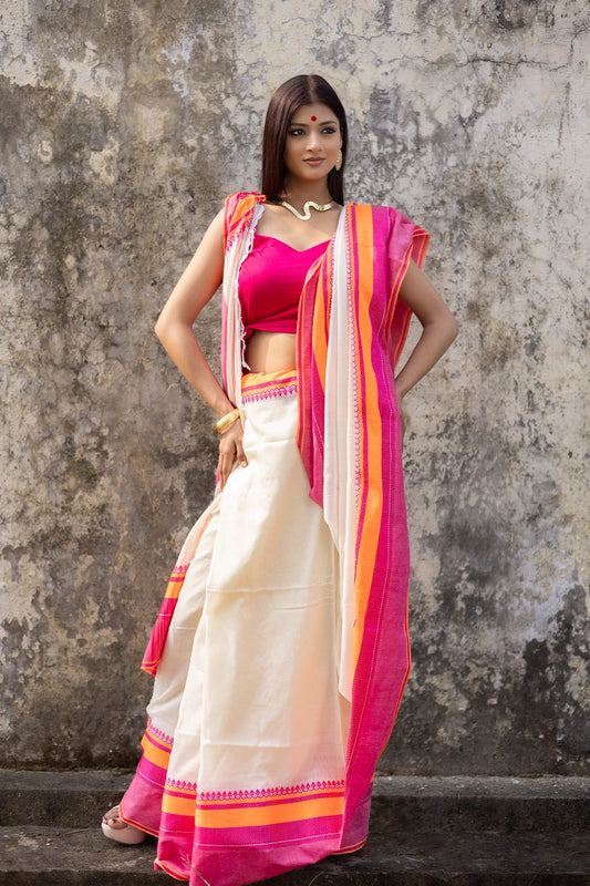 Woman wearing a traditional saree with pink and orange border against a textured wall.