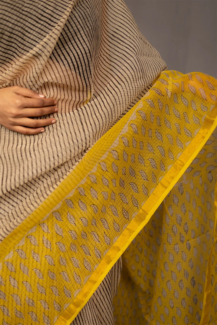 Woman wearing a beige and yellow saree with a grey background