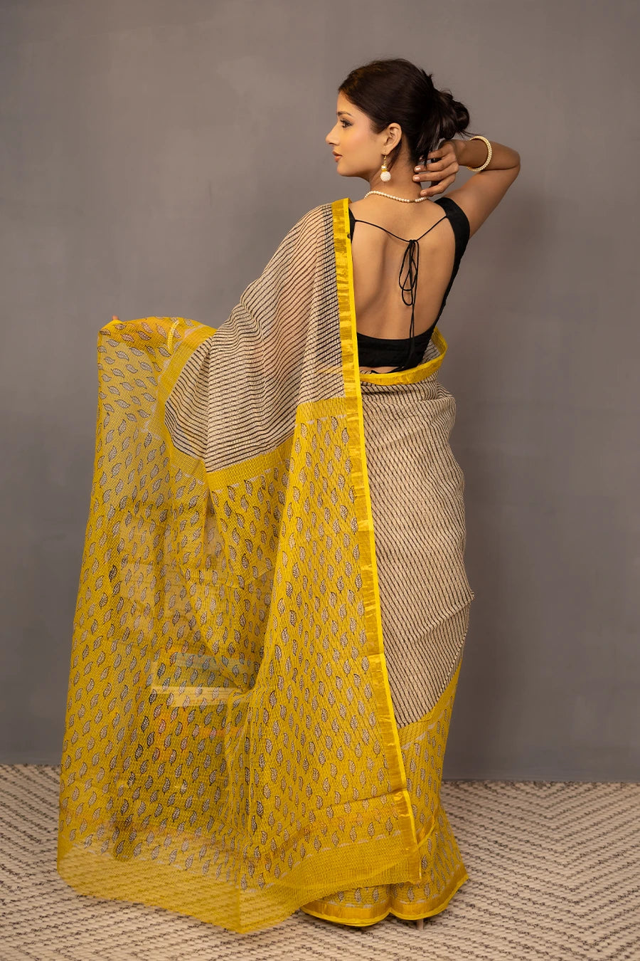 Woman wearing a beige and yellow saree with a grey background