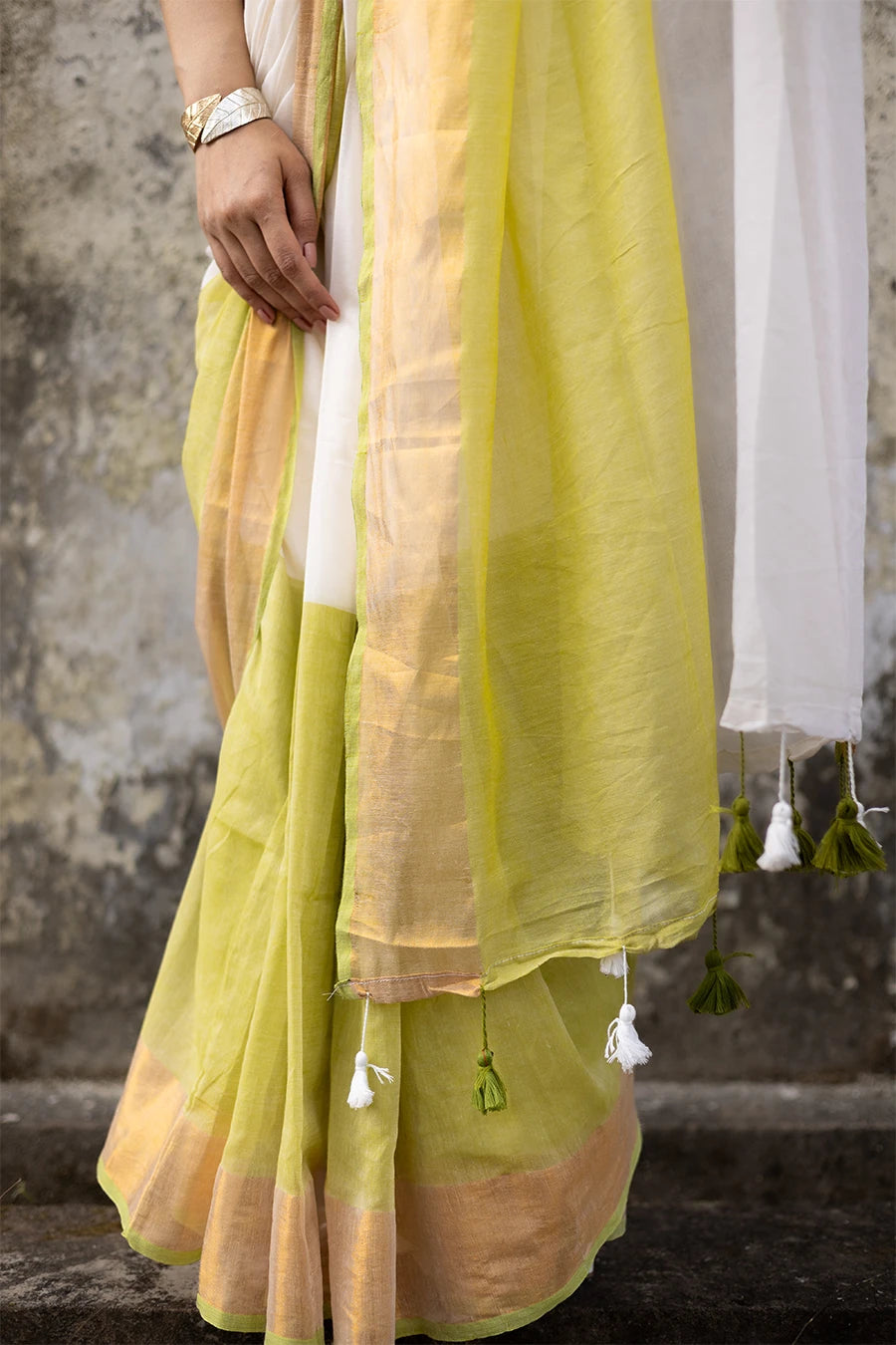 Woman wearing a white and yellow saree against a textured wall