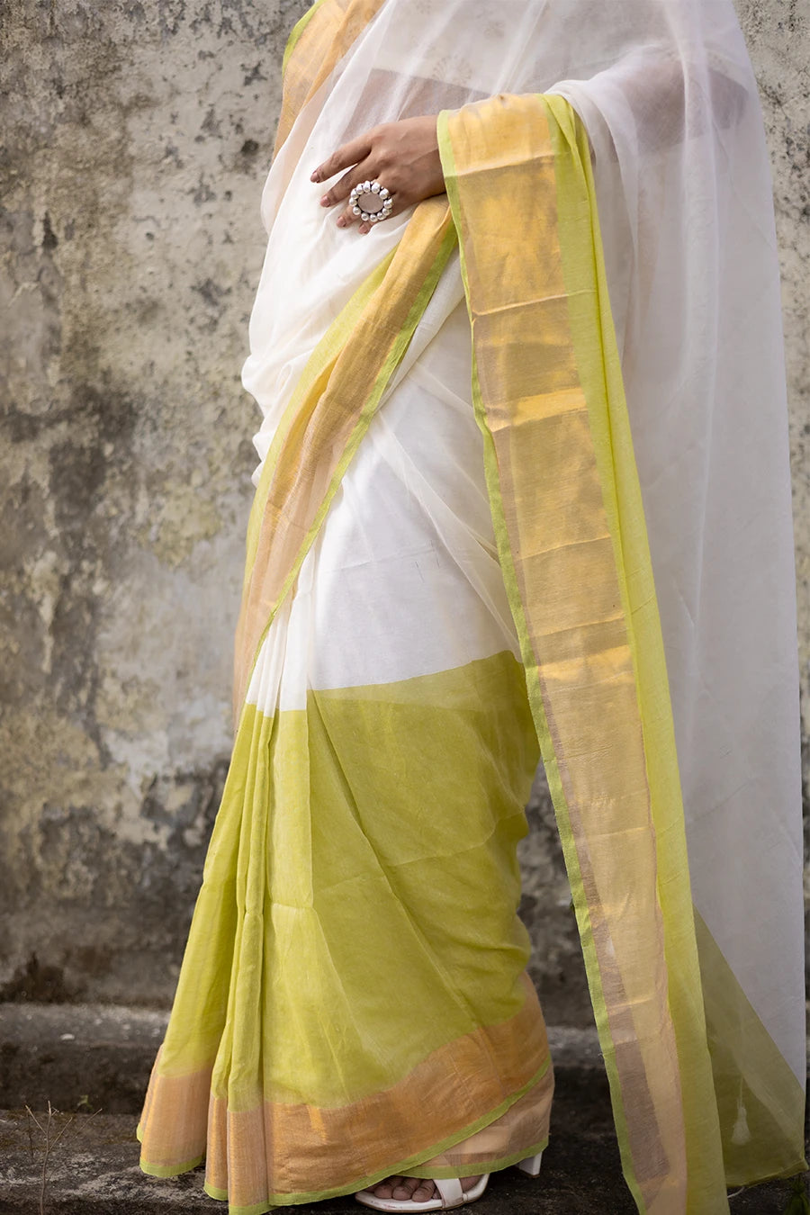 Woman wearing a white and yellow saree against a textured wall
