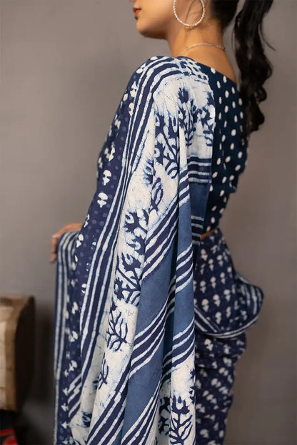 Woman wearing a blue saree with a pattern, standing next to a small table with books and a map.