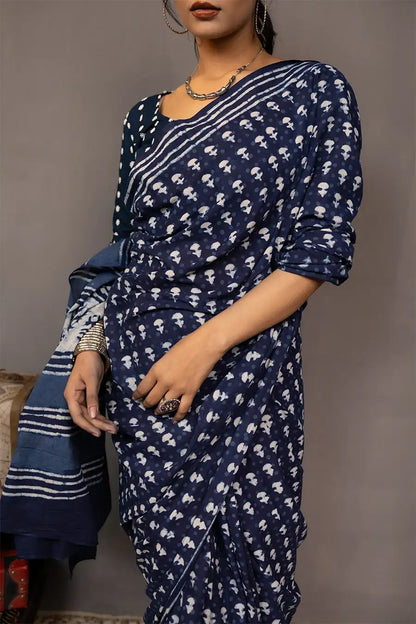 Woman wearing a blue saree with a pattern, standing next to a small table with books and a map.