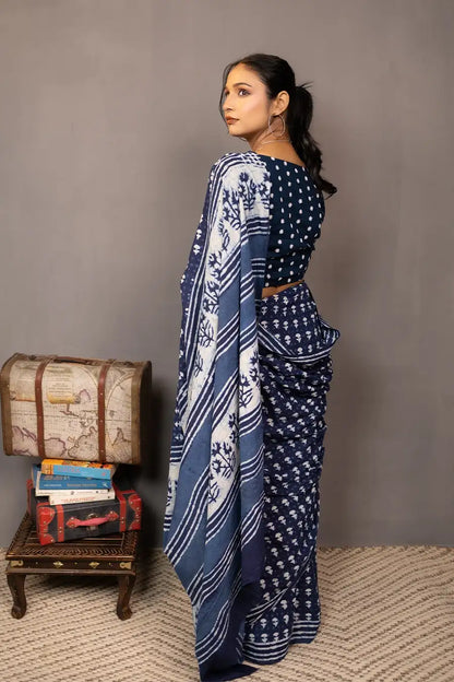 Woman wearing a blue saree with a pattern, standing next to a small table with books and a map.