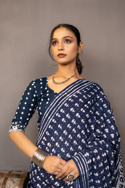 Woman wearing a blue saree with a pattern, standing next to a small table with books and a map.